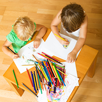 Children drawing on paper with colored pencils in a learning center.